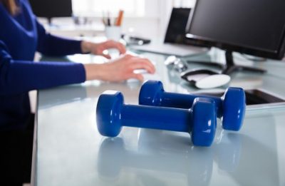 Close-up Of Two Blue Dumbbell In Front Of Businessperson Working In Office
